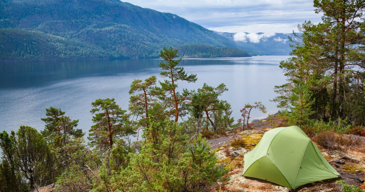 Green tent pitched up on a camping spot with a gorgeous lake view