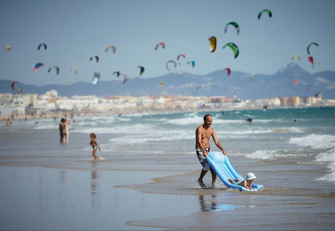 Man playing with his child on the beach surrounded by paragliders